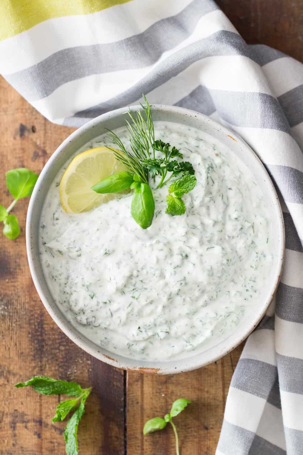 Bowl of Quark Dip viewed from the top garnished with herbs and sliced lemon on a wooden board and a grey and white napkin.