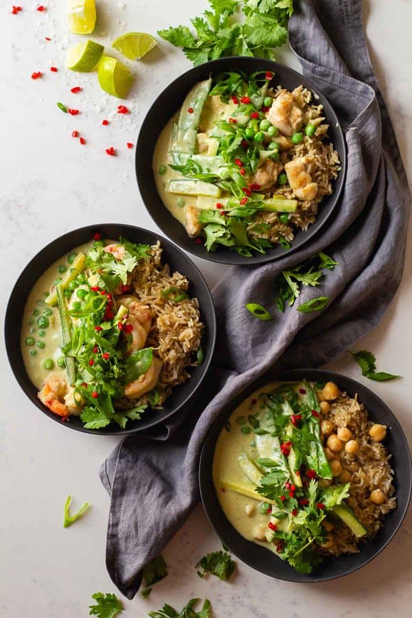 Three different types of Thai green curry in grey bowls. One with chicken, one with shrimp, and one with chickpeas.