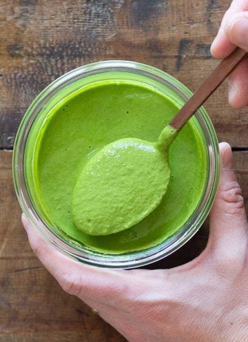Green tahini sauce in jar and spoon lifting up green sauce.