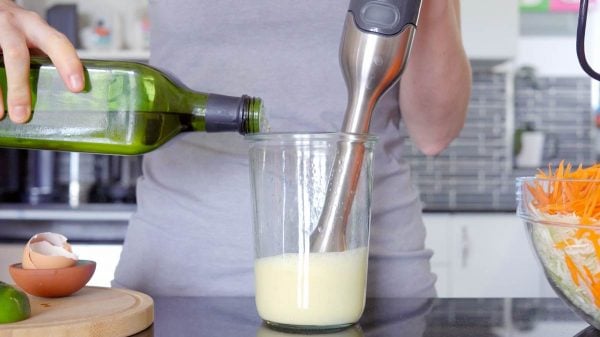 immersion blender in glass jar oil being poured into mayonnaise