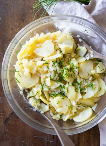 German Potato Salad in a glass salad bowl on a wooden table.