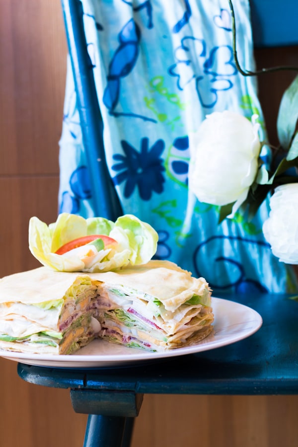 Sliced Crepe Cake on a plate on a blue table with a blue floral scarf in the background.