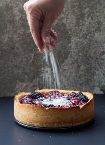Hand sprinkling sugar on a Healthy Berry Cake.