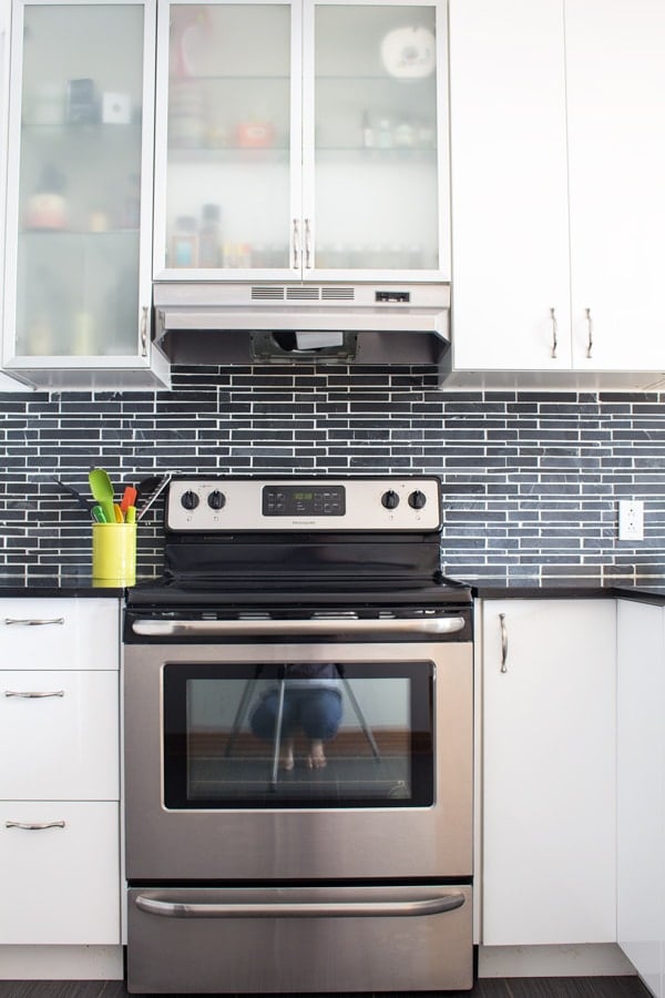 Front view of stainless steel stove, white kitchen cabinets and black backsplash.
