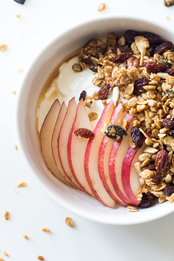 Top view of a bowl of yogurt topped with Healthy Homemade Granola, sliced apples and honey.