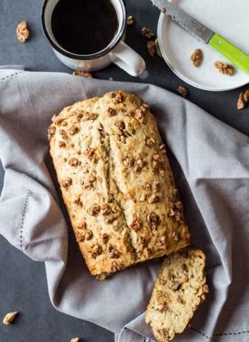 Top view of sliced Banana Bread with Maple Candied Walnuts, a cup of coffee, and an empty plate with a knife.