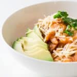 Close up of a bowl of Mexican Breakfast Chilaquiles con Camarones with shredded cheese and avocado slices.