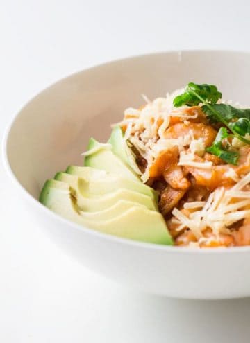Close up of a bowl of Mexican Breakfast Chilaquiles con Camarones with shredded cheese and avocado slices.