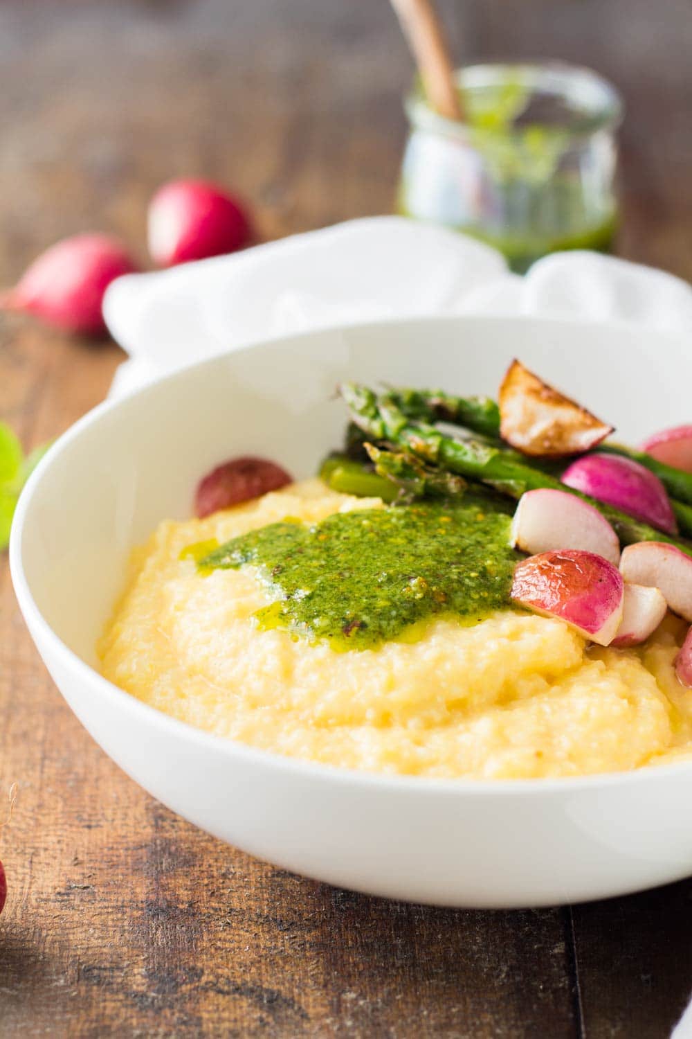 Close up of Creamy Parmesan Polenta with Grilled Vegetables and 5-Minute Basil Pistachio Pesto in a white bowl.