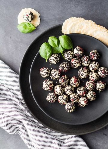 Top view of Easy Goat Cheese Appetizer on a black plate garnished with basil leaves, and a striped napkin.