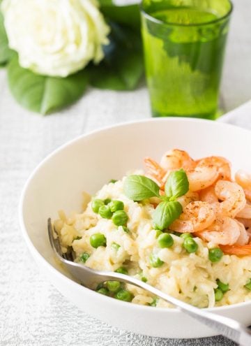Shrimp and Pea Risotto on a white plate with a fork, a glass of water and a flower.