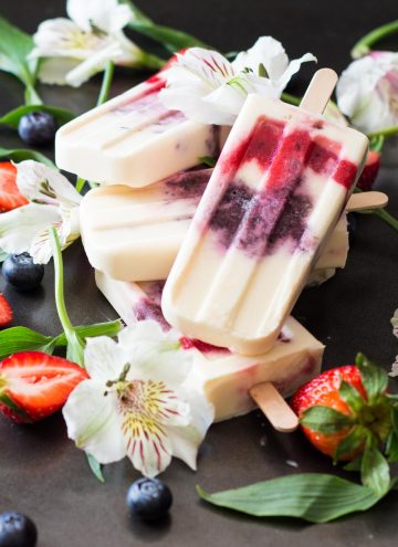 Close up of Greek Yogurt Berry Popsicles laid in a pile with fresh flowers, strawberries and blueberries.