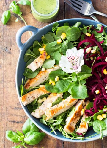 Top view of Watercress Salad with chicken, garnished with a flower, a jar of Basil Clementine Dressing.