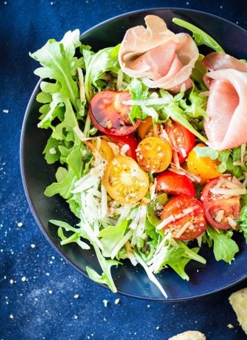Top view of Arugula Tomato Prosciutto Salad in a blue bowl.