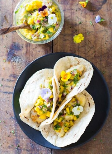 Top view of Easy Fish Tacos on a plate and a jar of Mango Salsa with a wooden spoon.