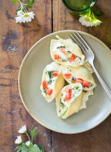 Spinach Ricotta Stuffed Shells on a plate with a fork, on a wooden table with flowers.