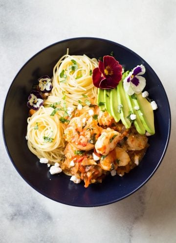 Top view of Mexican-Style Shrimp Capellini Pasta in a black bowl decorated with fresh flowers.