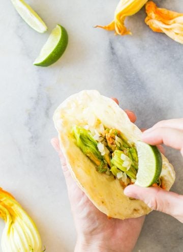 Hand holding a Squash Blossom Quesadilla and squeezing a lime on it.