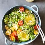 Top view of Mexican-Style Side Salad in a blue ceramic bowl with a fork and a spoon, and a jar of honey lime dressing.