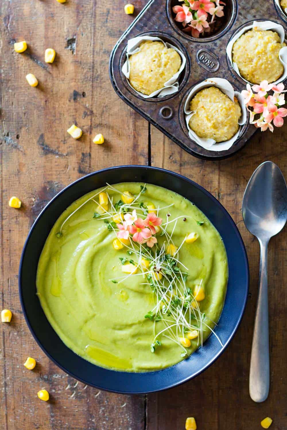 Top view of Vegan Cream Broccoli Soup, a spoon, and cornbread muffins in a muffin tin.