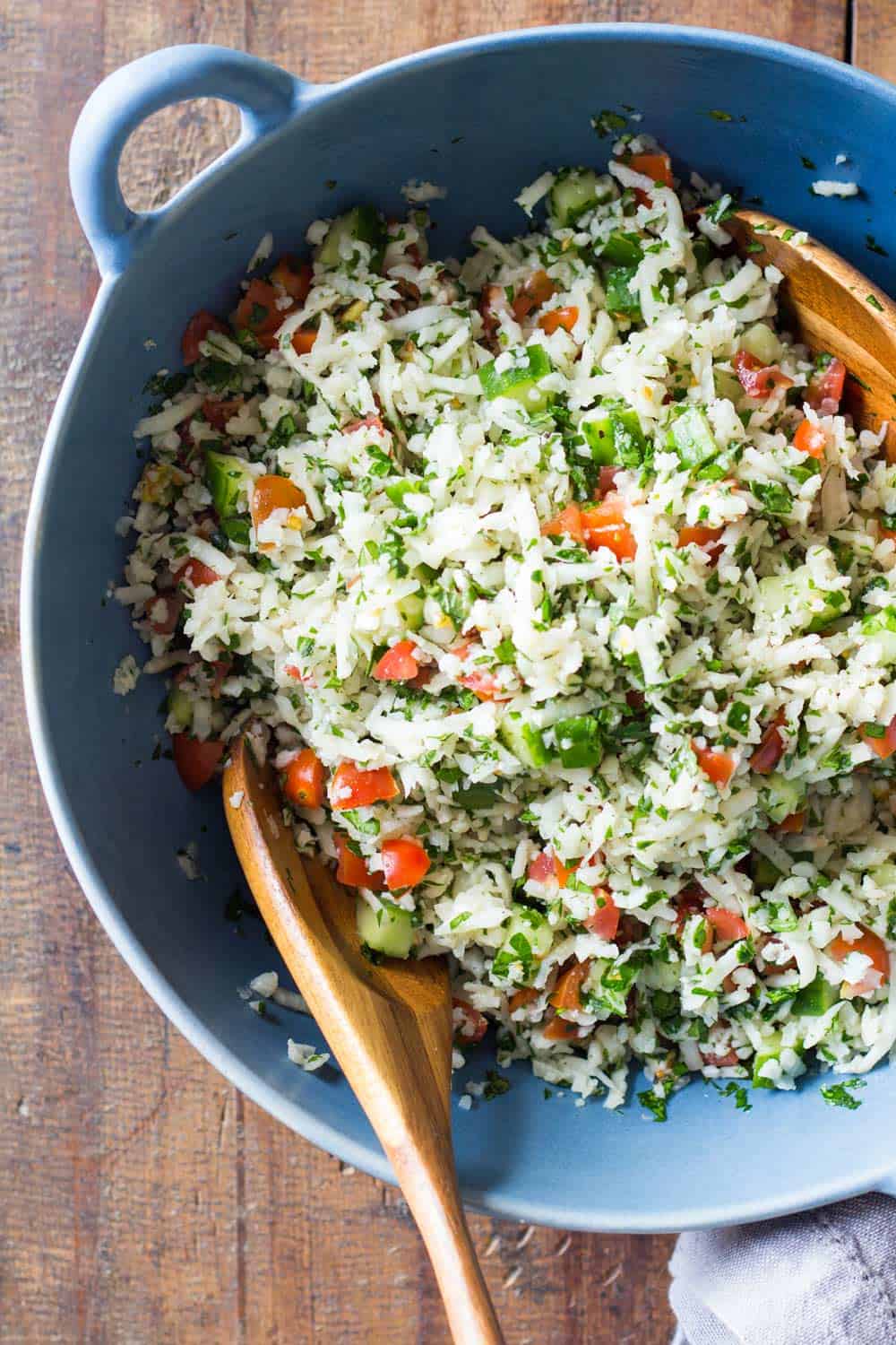 Cauliflower couscous tabbouleh salad in a blue bowl and two wooden spoons. 