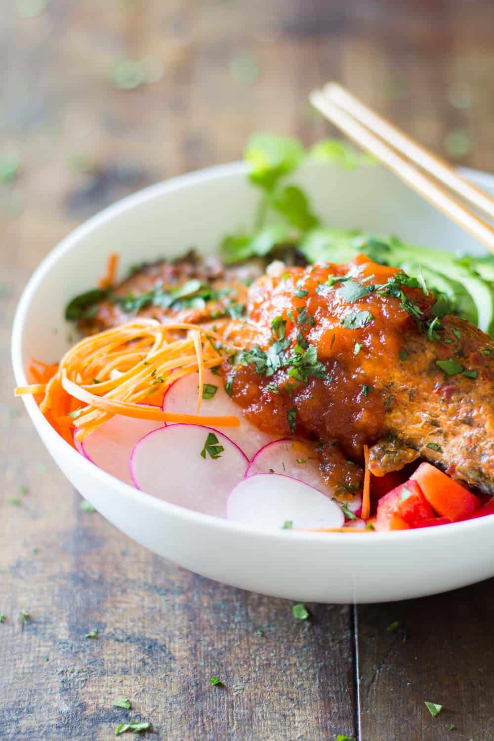 Salmon poke salad with peppers, radish, veggie noodles, wild rice and avocado, topped with sauce, served in a white bowl. 