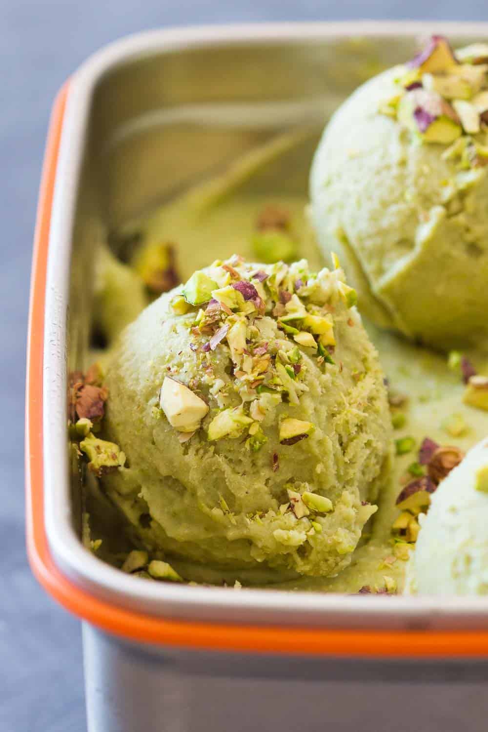 Texture of pistachio ice cream topped with chopped pistachio in a metalic bowl.