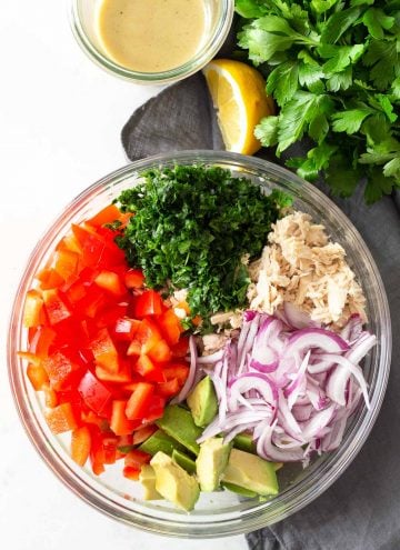 Avocado tuna Salad deconstructed in a large glass bowl on a grey napkin, with dressing on the side.