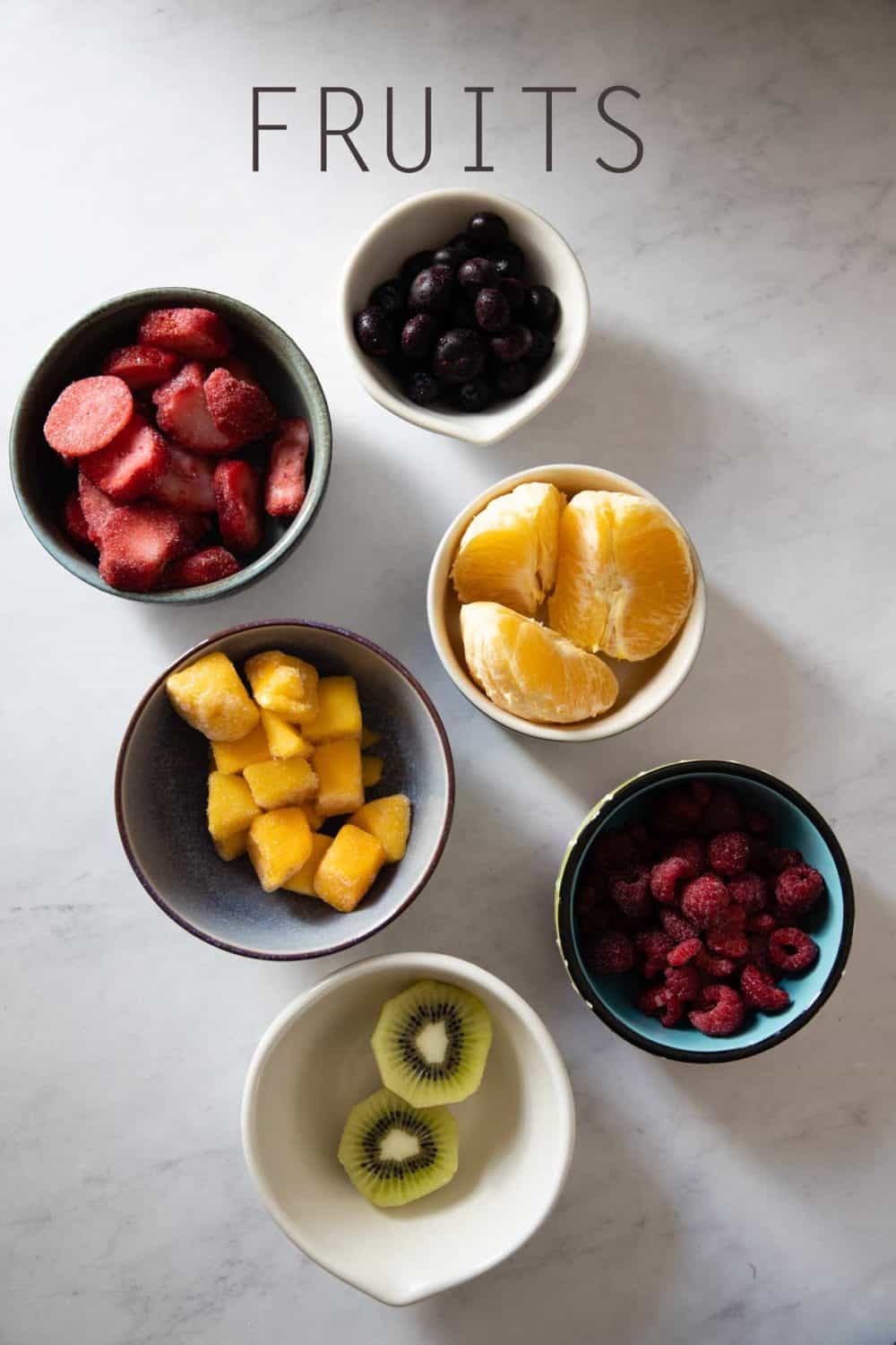 Kiwi, raspberries, mango, orange, strawberries, blueberries in bowls as example for best fruit for breakfast smoothies.