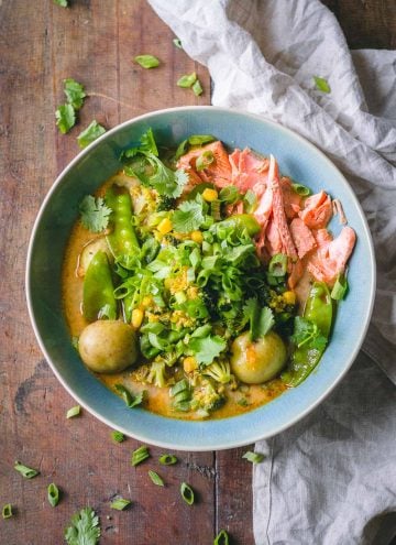 Thai Curry Soup in a blue bowl showing shredded salmon, potatoes, broccoli, and snow peas in broth on a wooden table