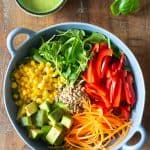 Ingredients for healthy summer salad with fresh vegetables in a light blue salad bowl, and a cup of orange basil vinaigrette.
