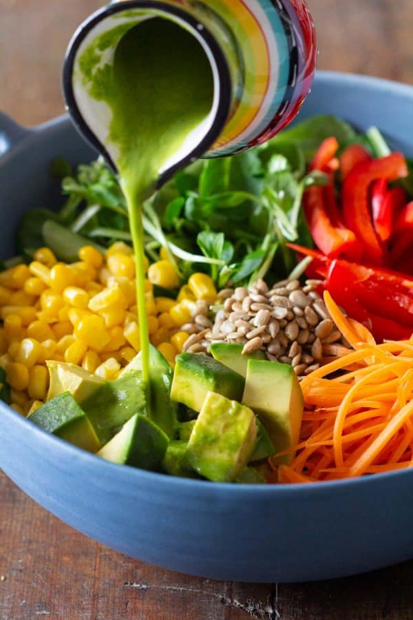 Homemade vinaigrette dressing being poured onto a seasonal summer salad.