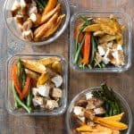 4 meal prep containers with cubed chicken, sweet potato wedges, potato wedges, asparagus, green beans, and bell pepper.