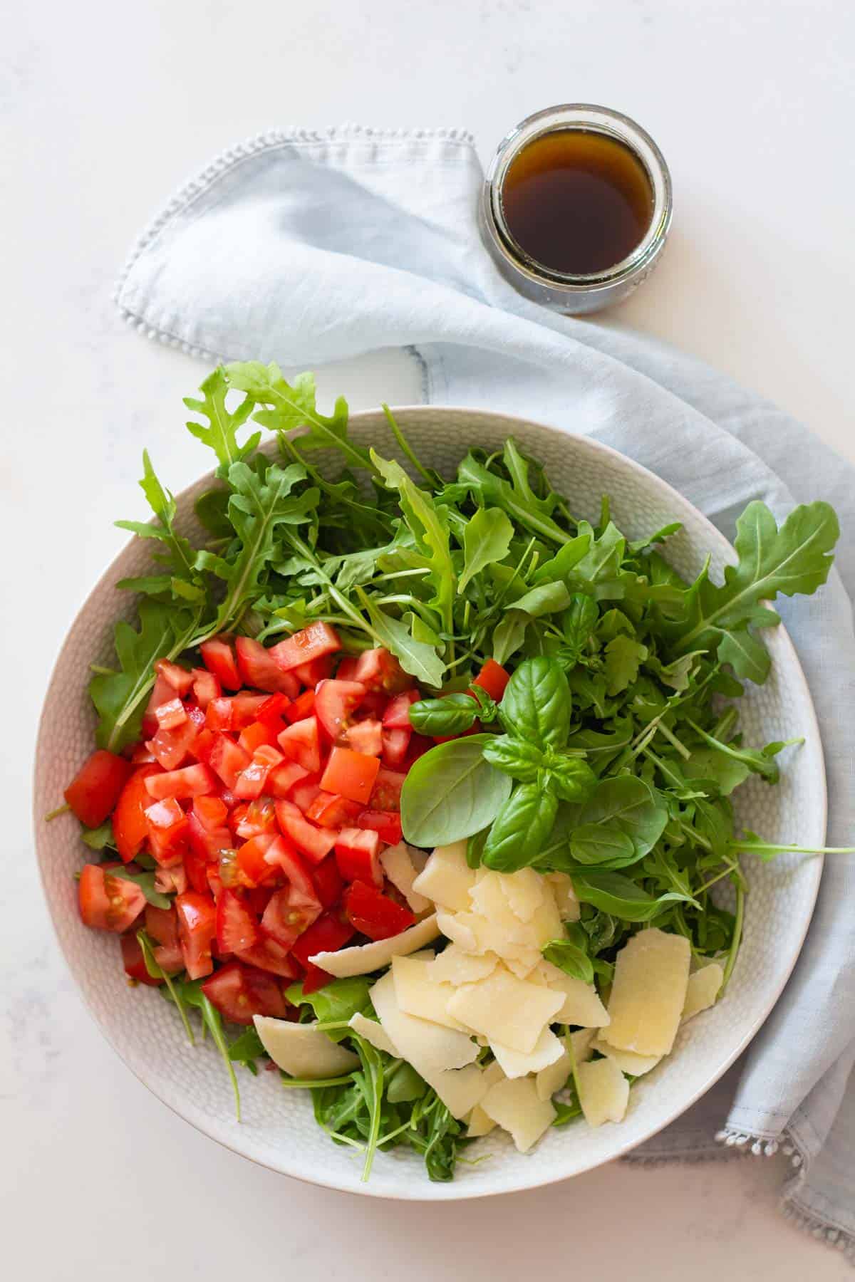 arugula, diced tomato, and shaved parmesan in a white salad bowl