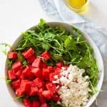 Watermelon and crumbled feta on top of arugula in a salad bowl