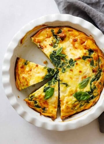 Crustless Spinach Quiche in a pie dish one piece missing two pieces cut out.