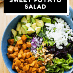 Lettuce, roasted sweet potato, avocado, onion, feta, cranberries in a blue salad bowl, dressing on the side with text overlay for Pinterest.