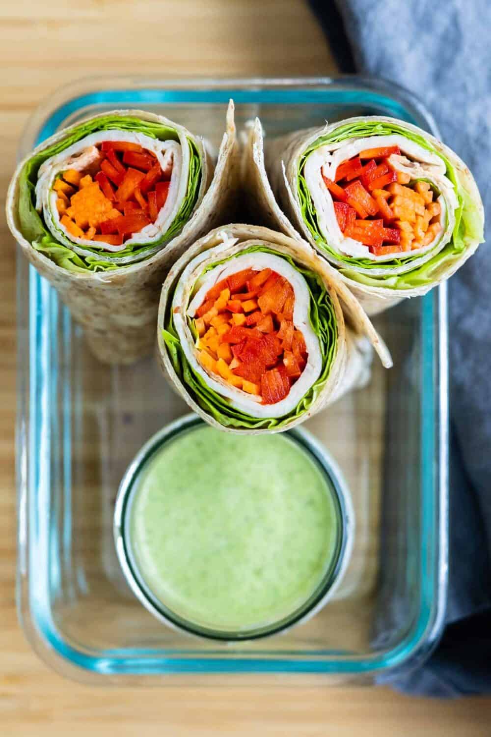 turkey wraps cut open and in a glass bowl next to green sauce in another bowl.