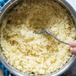 Stainless steel pot with cooked couscous and fork inside fluffing the couscous.