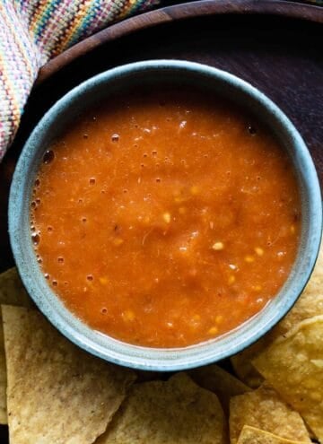 salsa roja in a blue bowl surrounded by tortilla chips.