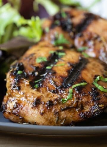 close-up image of a piece of balsamic grilled chicken thigh on a grey plate with salad in the background.