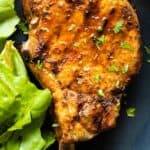 Grilled pork chop on a plate and green lettuce on the side.