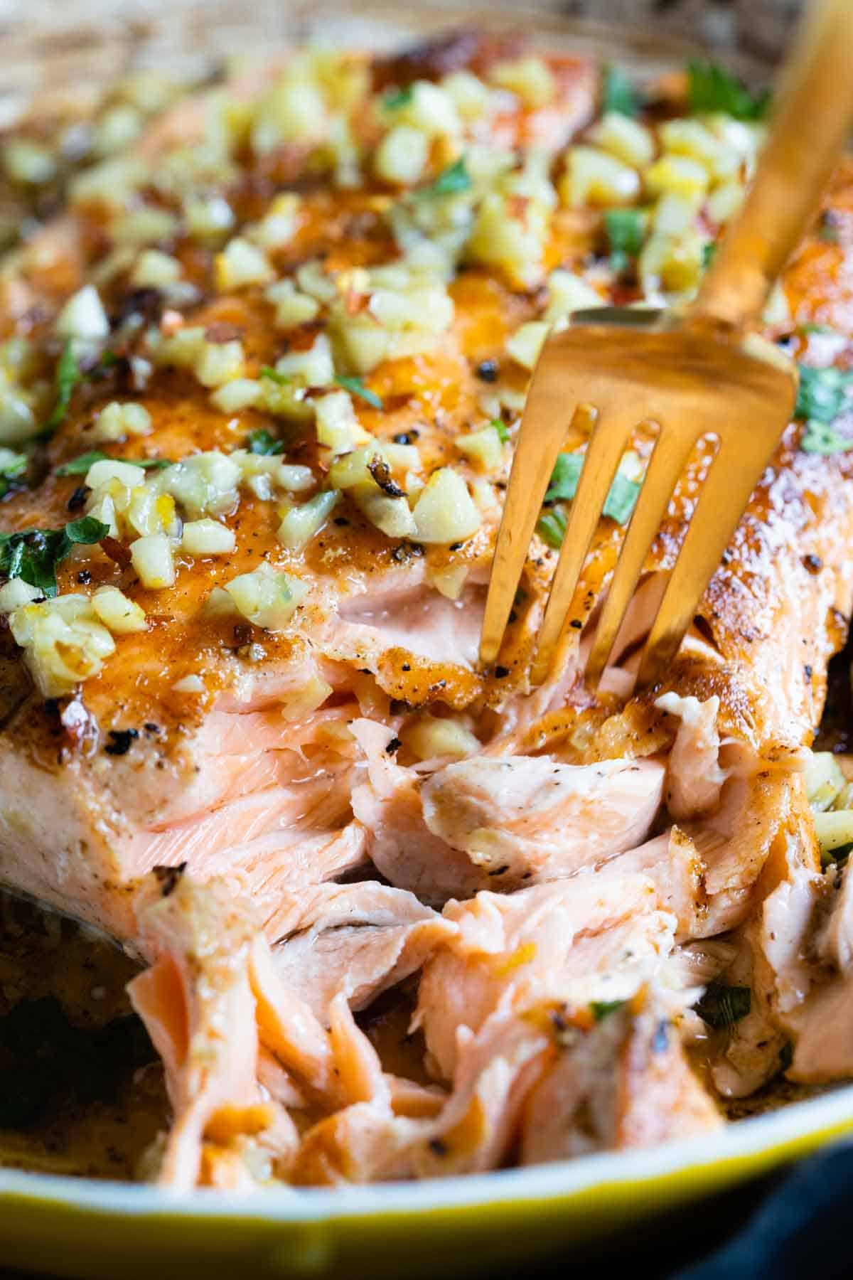 Closeup showing texture of cooked pan-seared salmon with garlic on top.