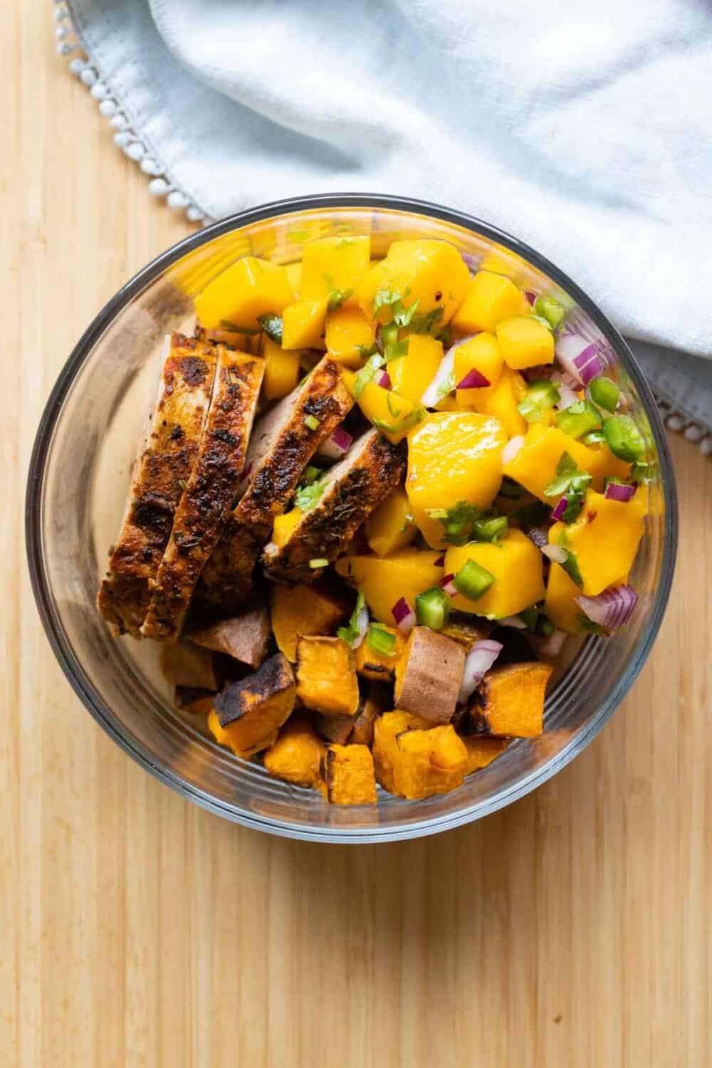 Round glass meal prep bowl filled with pork, mango, and sweet potato.