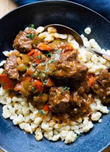 German Goulash on top of Spaetzle in a blue soup bowl.