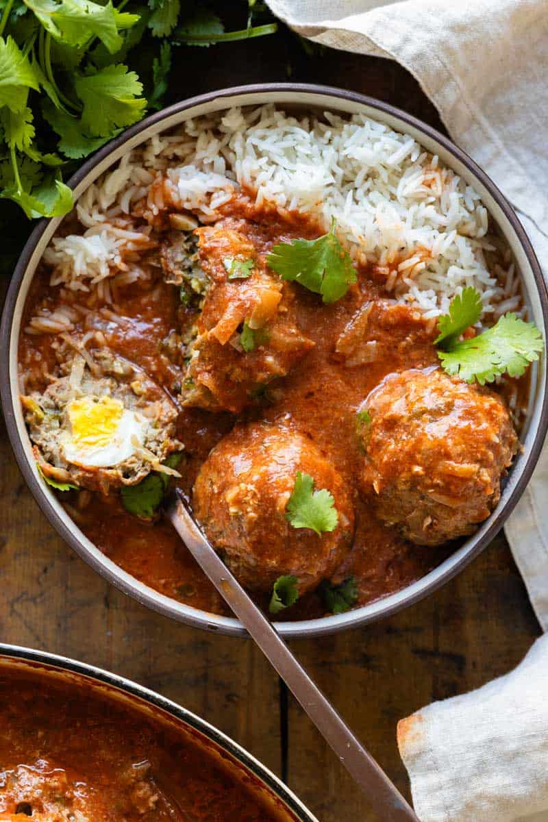 Albondigas in tomato sauce served over white rice and sprinkled with cilantro in a bowl. One meatball cut open to show the egg inside.