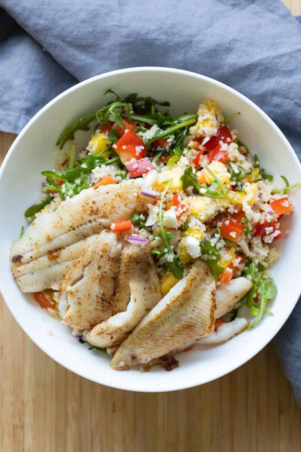 A white bowl filled with couscous salad and fried sole fillets.